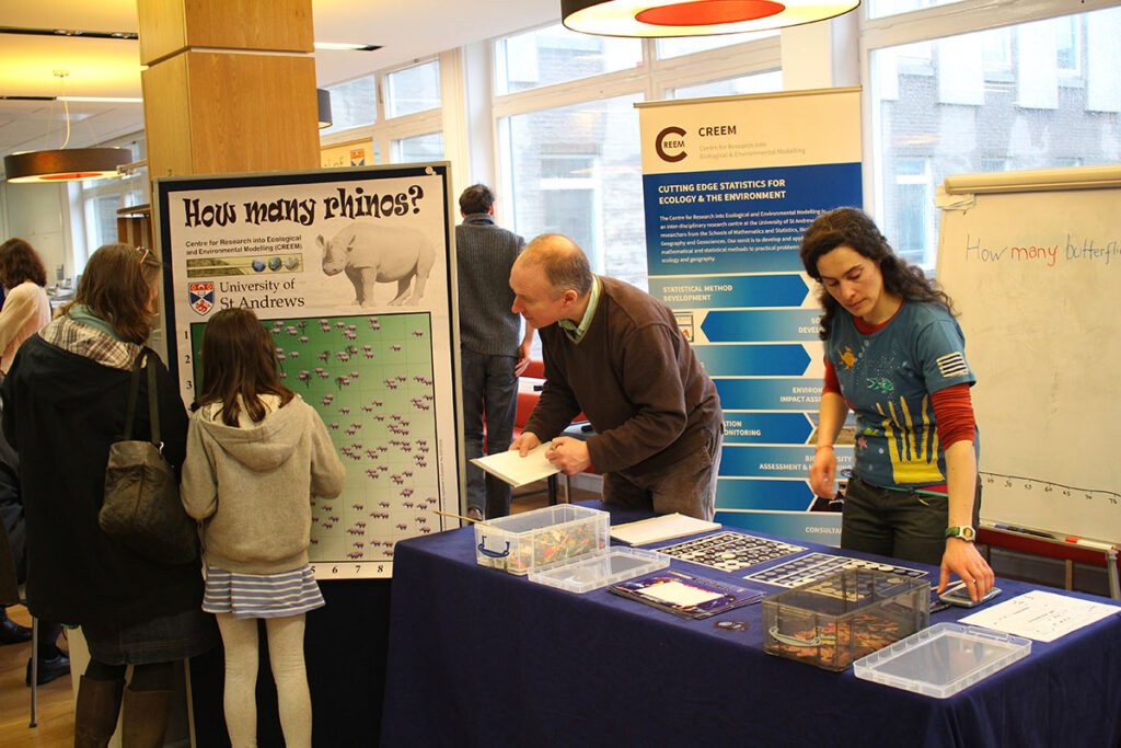 Visitor looking at poster about rhinos, and a researcher explaining some of the details